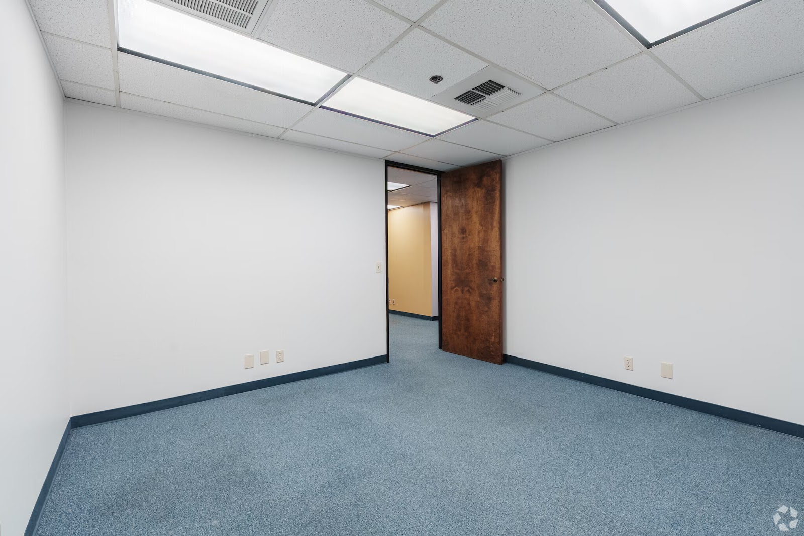 Private 200 SF interior office space for lease at 200 New Stine Building in Bakersfield CA with blue carpet and wood grain door.